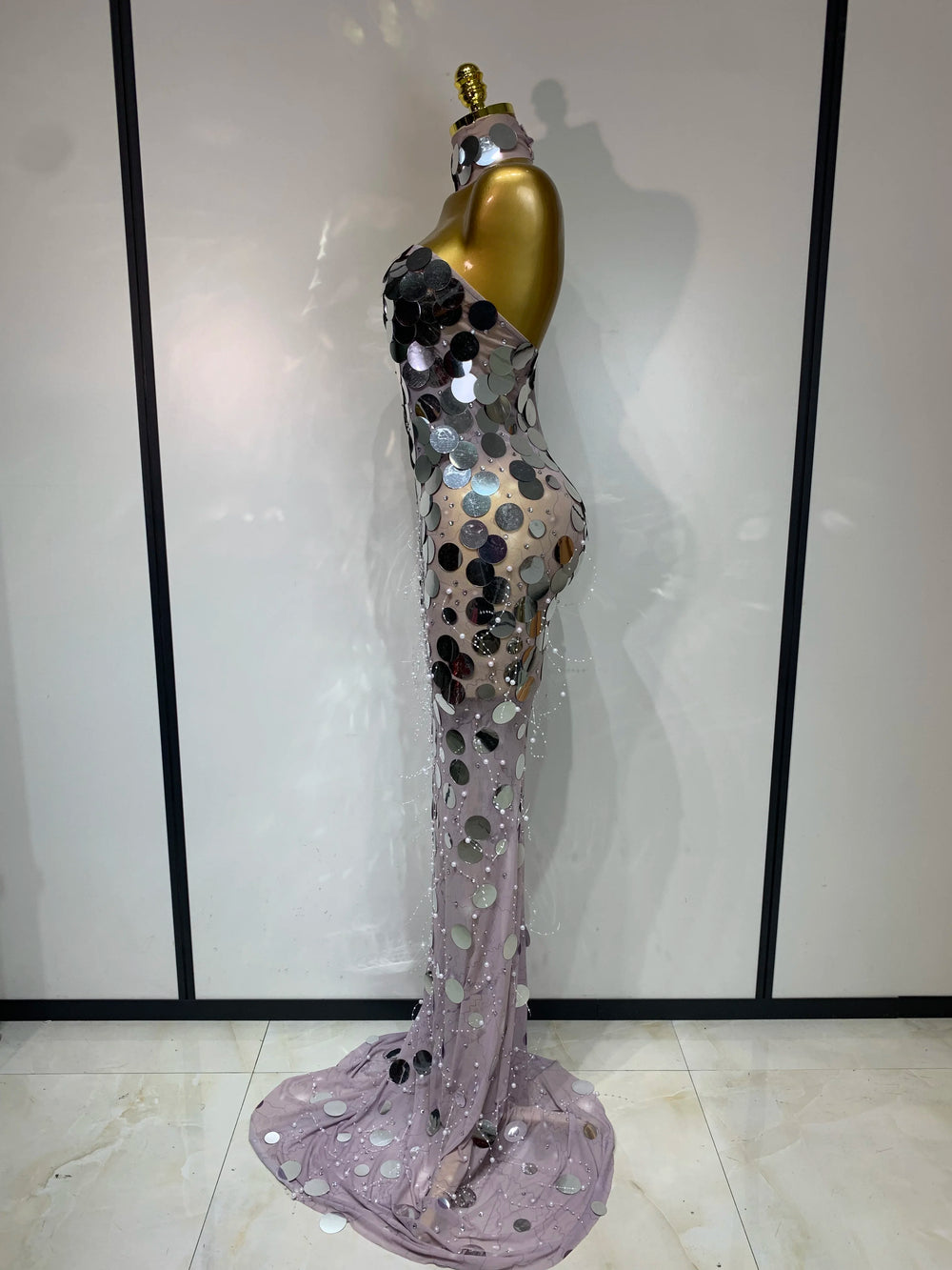 Elegant evening gown with sequins and beads on a mannequin against a white wall.