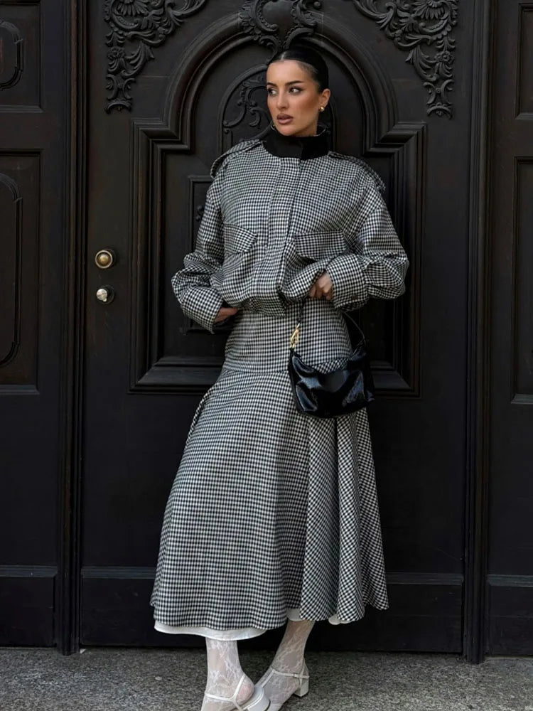 Woman in a checkered outfit standing in front of a dark door.