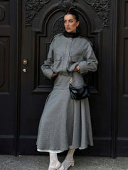 Woman in a checkered outfit standing in front of a dark door.