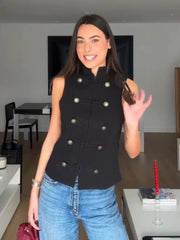 Woman wearing a black sleeveless jacket with gold buttons in a living room.