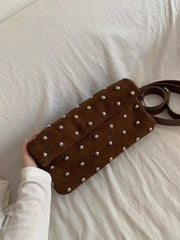 Brown studded handbag held by a person on a white bed