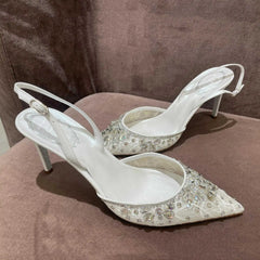 Pair of white high-heeled shoes with crystal embellishments on a brown surface