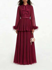 Burgundy pleated maxi dress with bow neck and feather trim