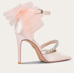 Pink high-heeled shoe with a large bow and embellishments on a light background