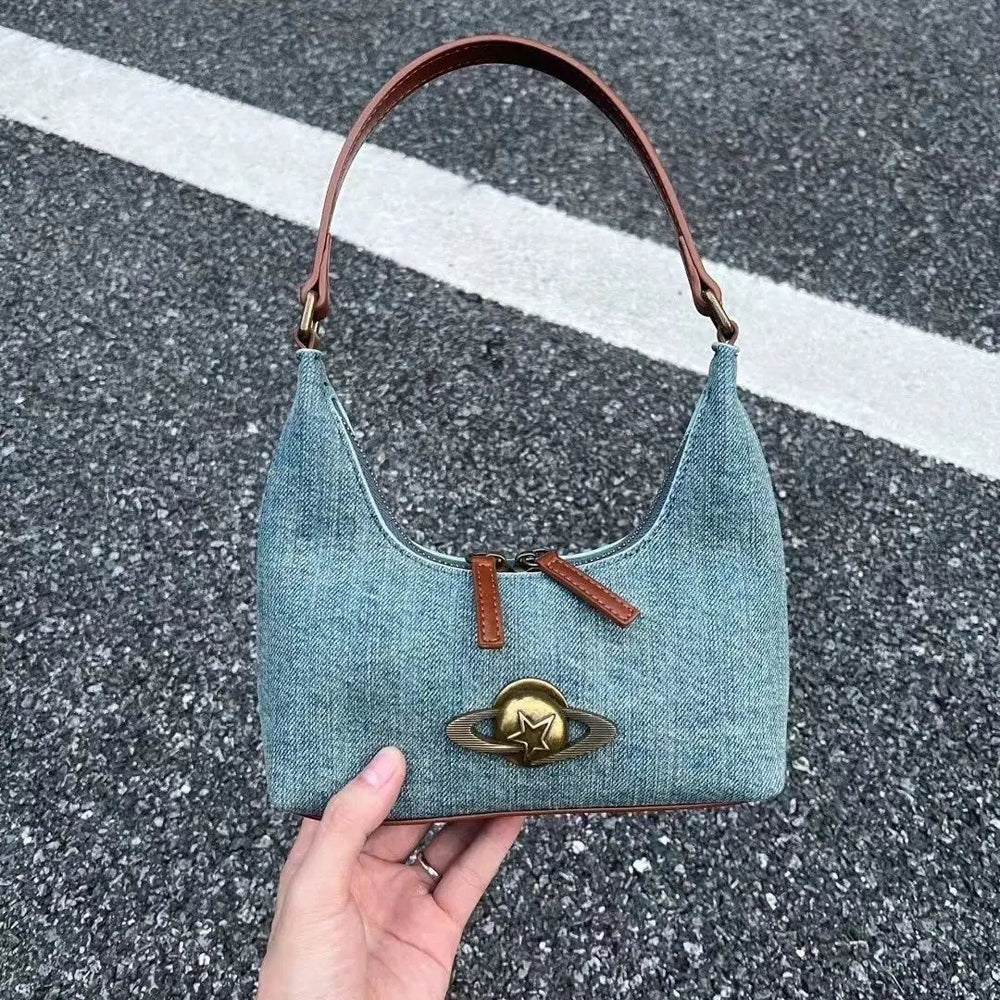Denim handbag with brown handle and star emblem held by a hand on a road surface