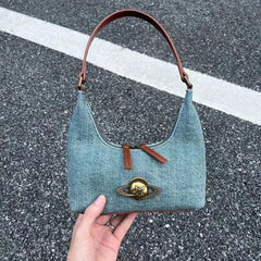 Denim handbag with brown handle and star emblem held by a hand on a road surface