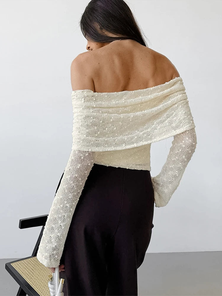 Woman wearing a white off-shoulder top with long sleeves against a plain background