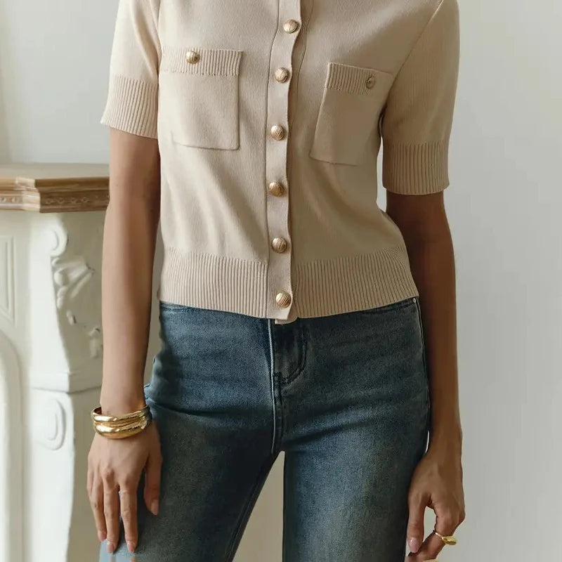Person wearing a beige cardigan with gold buttons and blue jeans indoors.