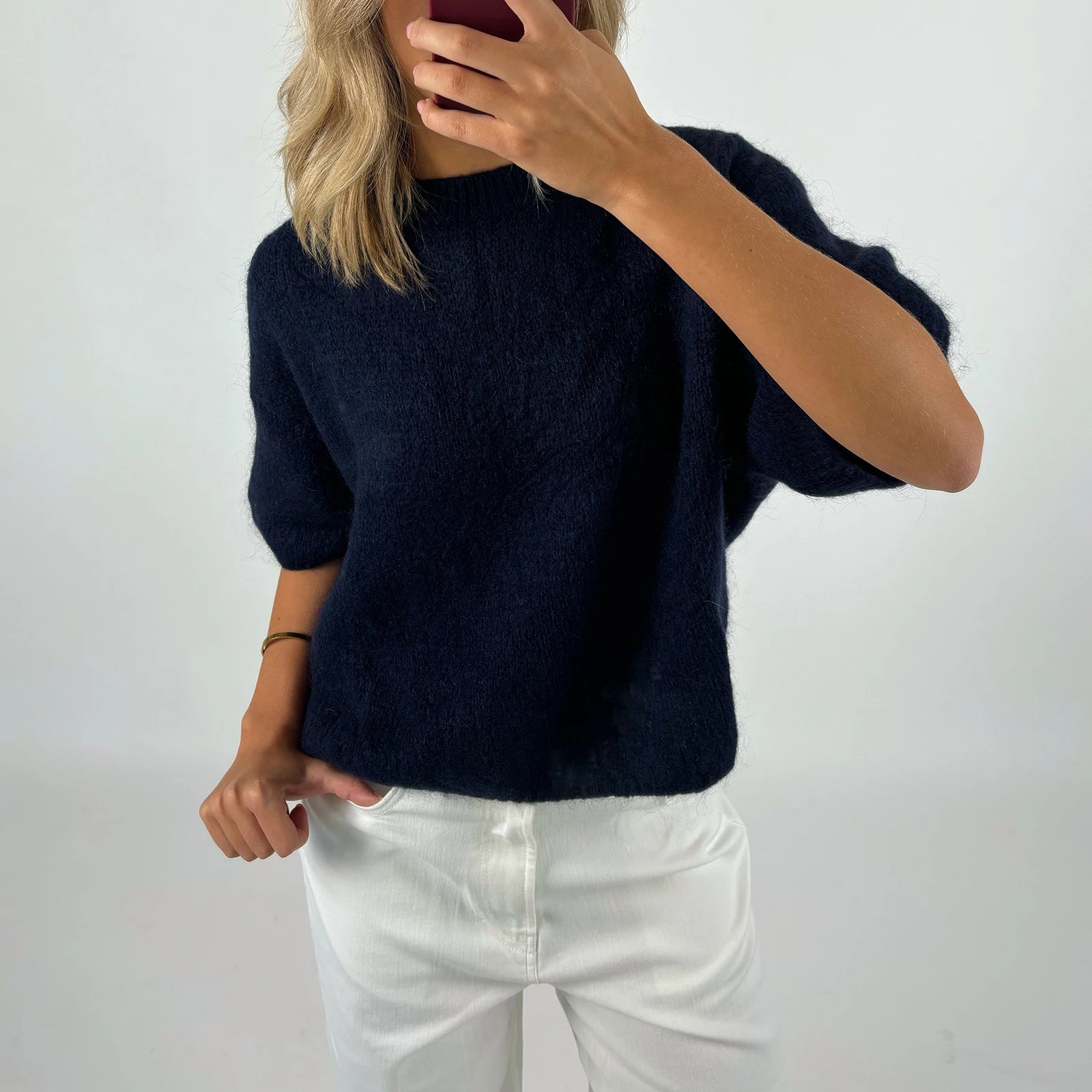 Person wearing a navy sweater and white pants against a plain background