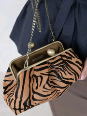 Clutch bag with tiger stripe pattern held by a person wearing a navy blue outfit.