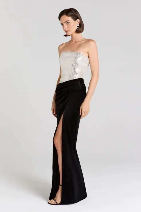 Side view of a strapless sequined bodice and velvet maxi skirt with a high slit