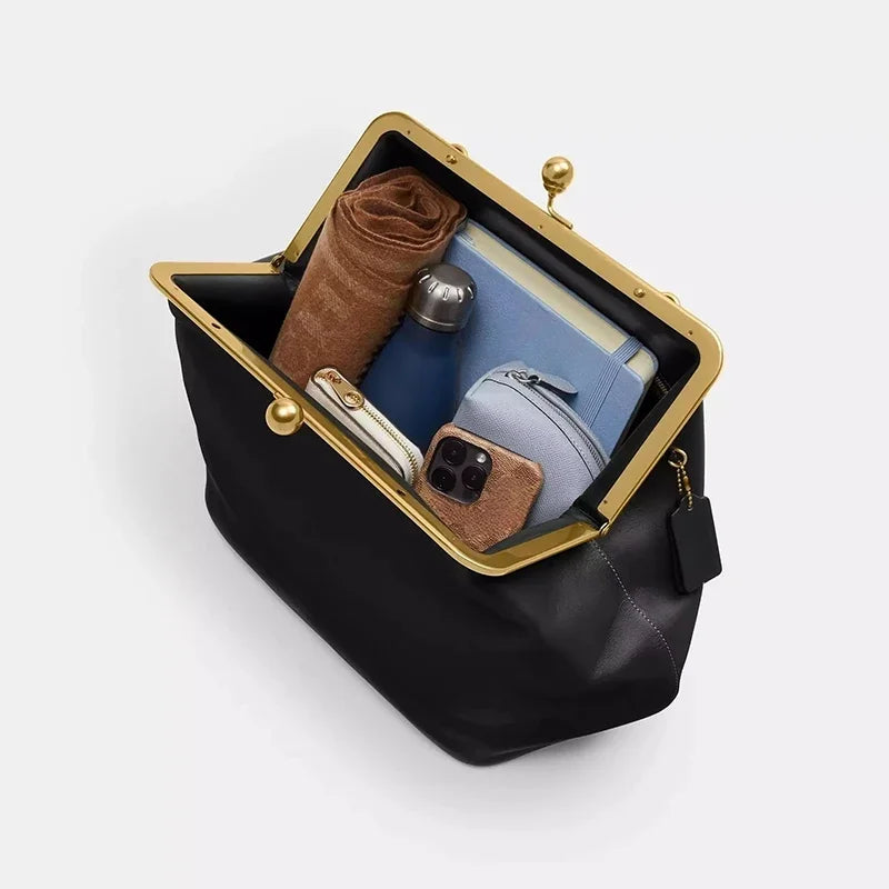 Black handbag with gold clasp containing a phone, wallet, and other items on a white background