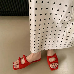 Red sandals worn with a white skirt featuring black polka dots on a neutral background