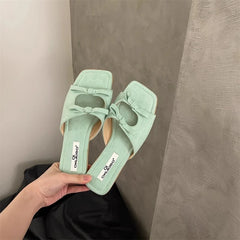 Light green sandals with bow detail held by a hand against a neutral background