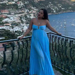 Woman in a blue dress standing on a balcony overlooking a coastal town with boats on the water.