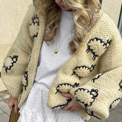 Person wearing a beige knitted cardigan with black sheep patterns.