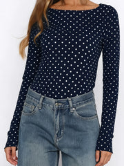 Person wearing a navy blue long-sleeve top with white polka dots and blue jeans on a white background