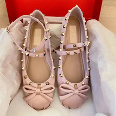 Pink studded ballet flats with bow detail and ankle strap.
