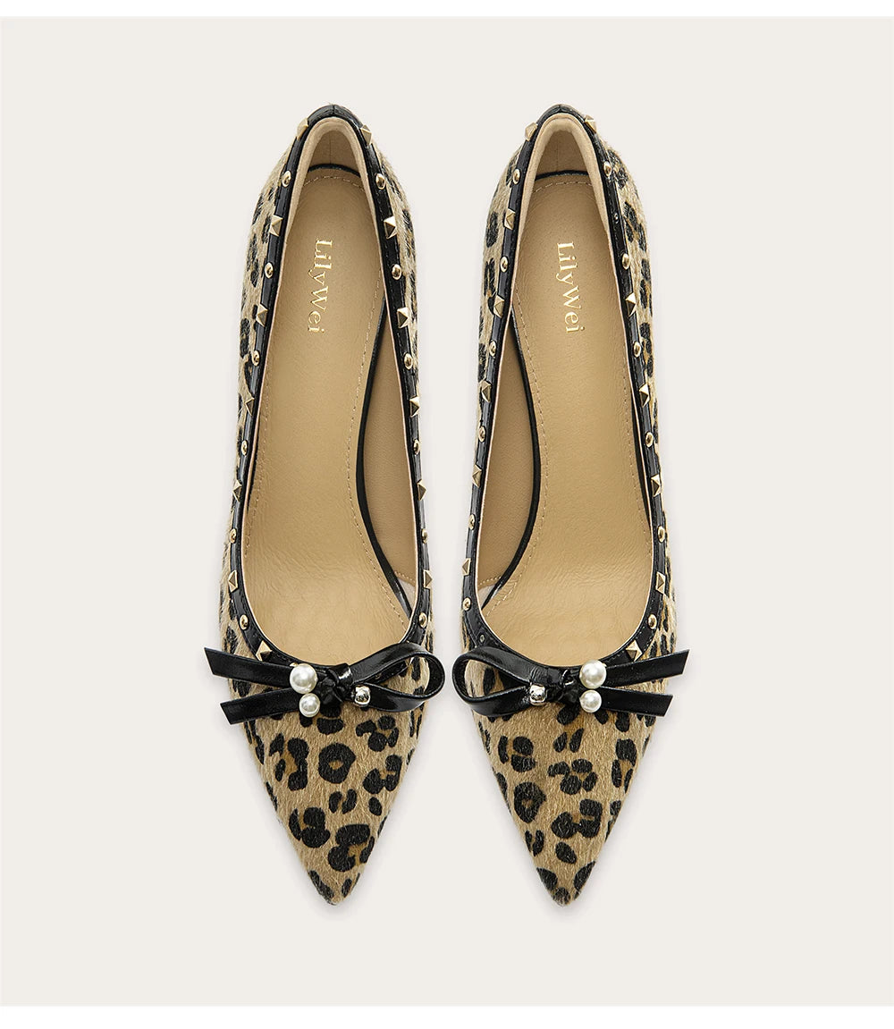 Pair of leopard print pointed-toe shoes with black bows and pearl decorations on a light background.