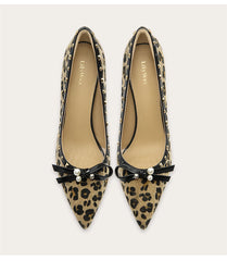Pair of leopard print pointed-toe shoes with black bows and pearl decorations on a light background.