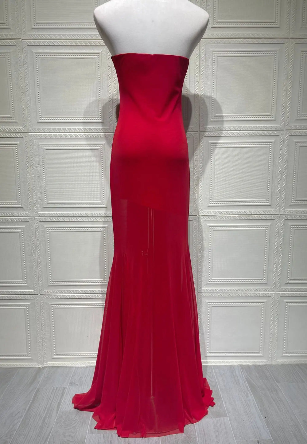 Red strapless evening gown on a mannequin against a white paneled wall.