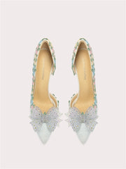 Pair of high-heeled shoes with floral straps and decorative bows on a light gray background