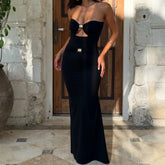 Woman wearing a black strapless gown with cut-out design in front of a stone building.