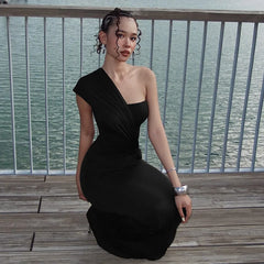 Woman in a black one-shoulder dress sitting on a wooden deck with water in the background