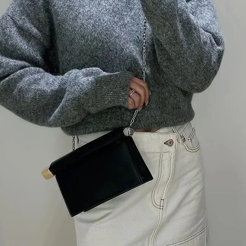 Person wearing a gray sweater and light-colored pants holding a black clutch bag.