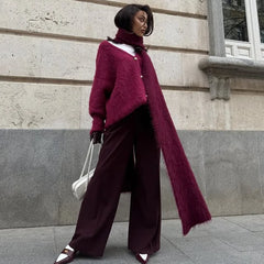 Woman wearing a long burgundy coat and wide-leg pants standing against a building.