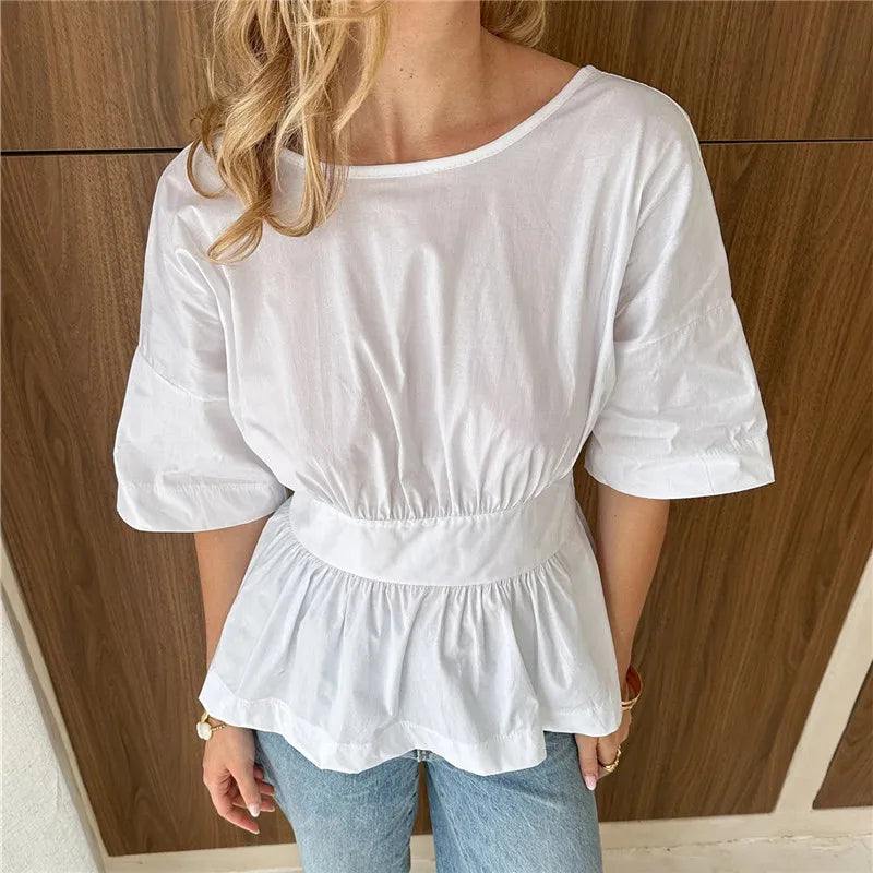 White blouse with ruffled details worn by a person against a wooden panel background