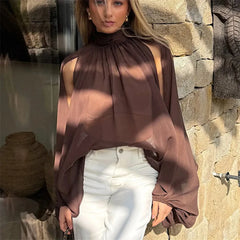Woman wearing a brown blouse and white pants standing against a stone wall.