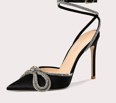 Black high-heeled shoe with decorative strap and embellishments on a white background