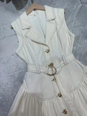 White sleeveless dress with gold buttons on a textured gray surface