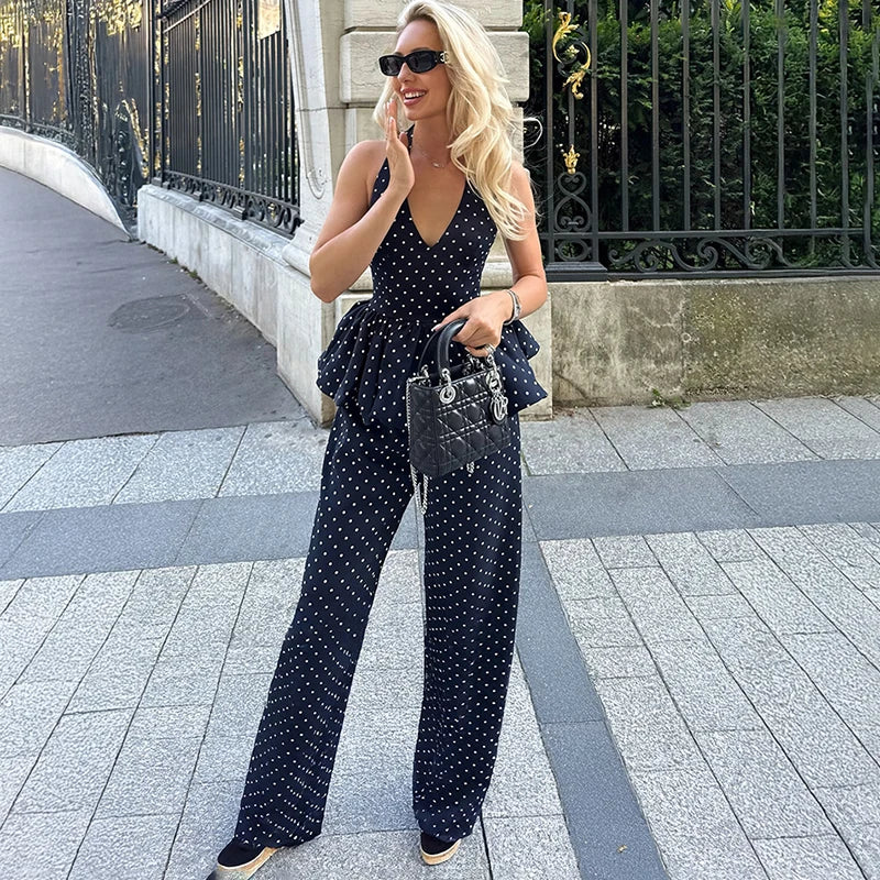Woman in a navy blue polka dot jumpsuit walking on a sidewalk.