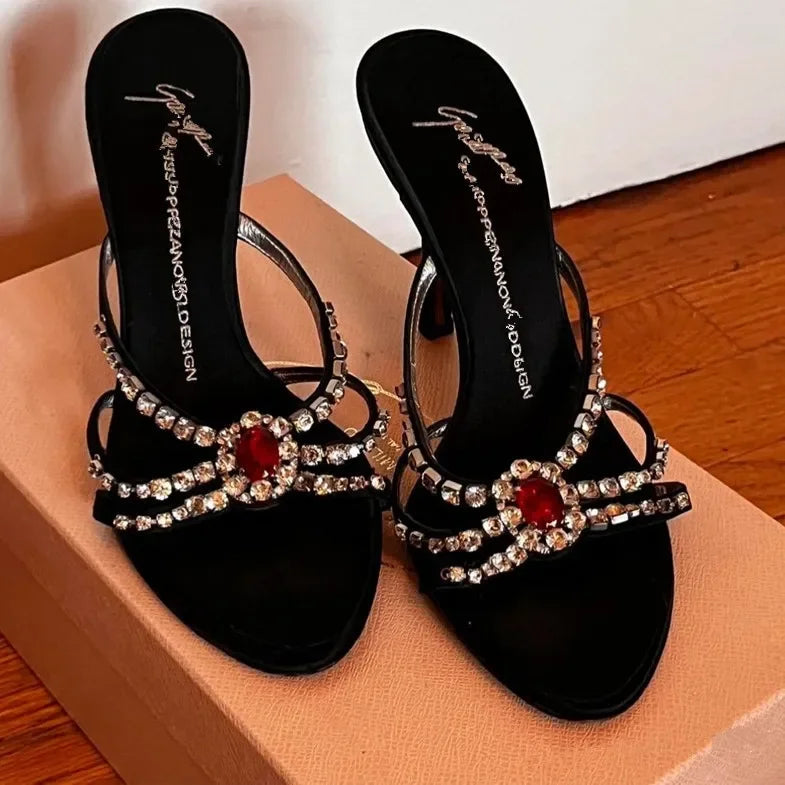 Pair of black open-toe stiletto heels with red spider gem embellishments.
