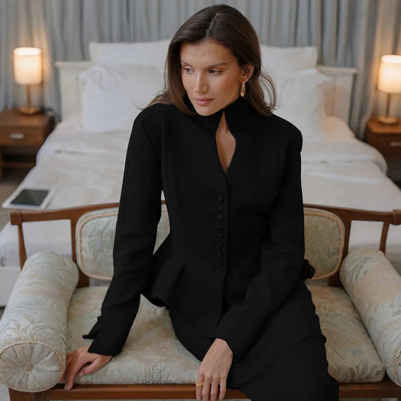 Woman in a black outfit sitting on a couch in a bedroom setting