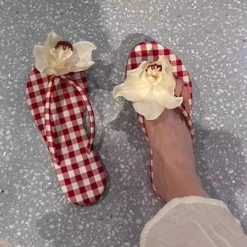 Red and white checkered slippers with floral design on a gray surface
