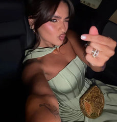 Woman in a green dress sitting in a car, pointing at the camera.