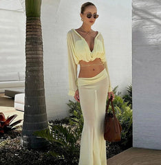 Woman in a yellow outfit standing outdoors with a palm tree and white wall in the background