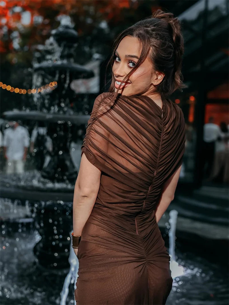Woman in a brown dress standing in front of a fountain with blurred people in the background