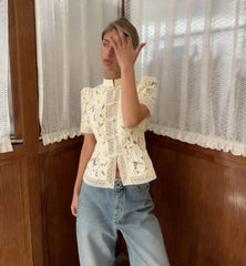 Person wearing a white lace top and light blue jeans in front of a window with white curtains.