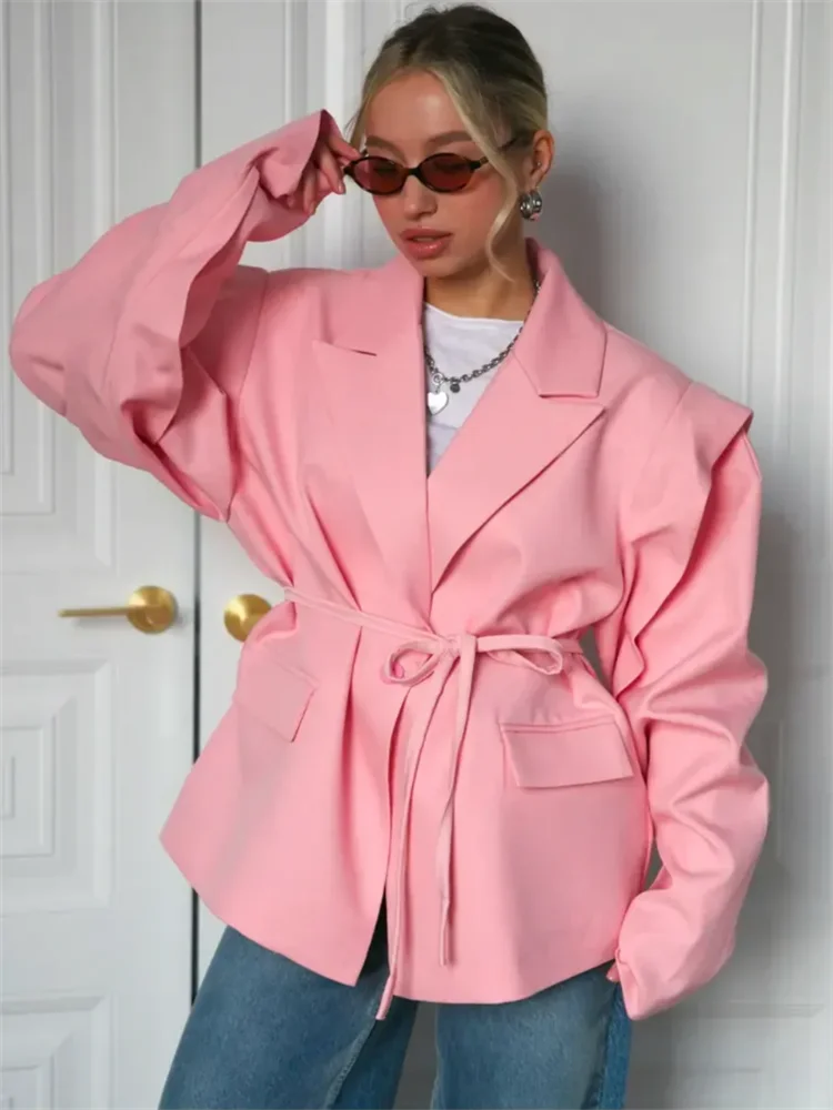 Person wearing a pink blazer with a white wall background