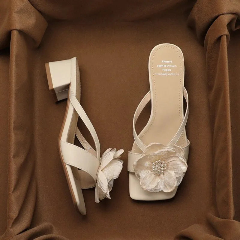 Pair of beige high-heeled sandals with floral decorations on a brown fabric background