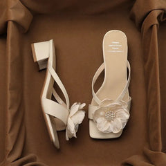 Pair of beige high-heeled sandals with floral decorations on a brown fabric background
