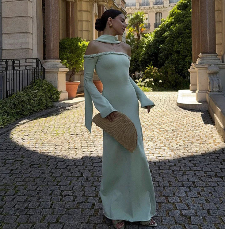 Woman in a light green dress standing on a cobblestone path with classical architecture in the background.