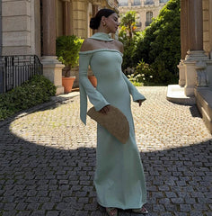 Woman in a light green dress standing on a cobblestone path with classical architecture in the background.