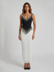 Full length view of a black beaded V-neck sleeveless top paired with a white ruched floor-length skirt.