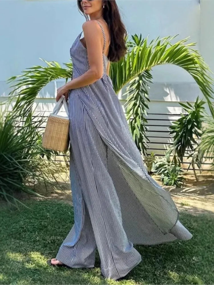 Woman in a long, light-colored dress standing outdoors with greenery and a clear sky in the background.