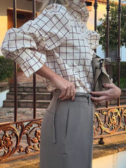 Person wearing a checkered blouse and holding a handbag on a balcony.